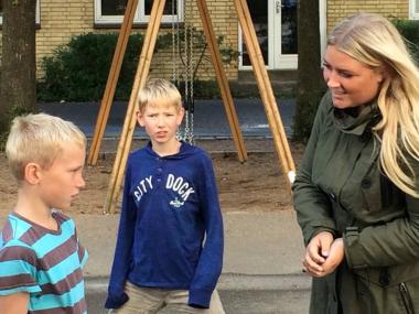 Kvindelig pædagog snakker med to drenge i skolegården
